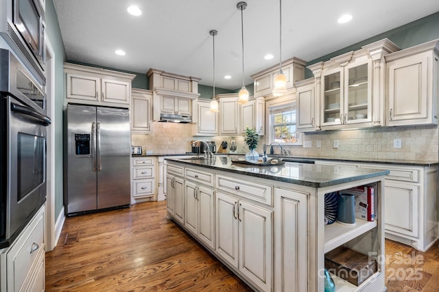 kitchen with pendant lighting, a center island, stainless steel appliances, decorative backsplash, and dark stone countertops