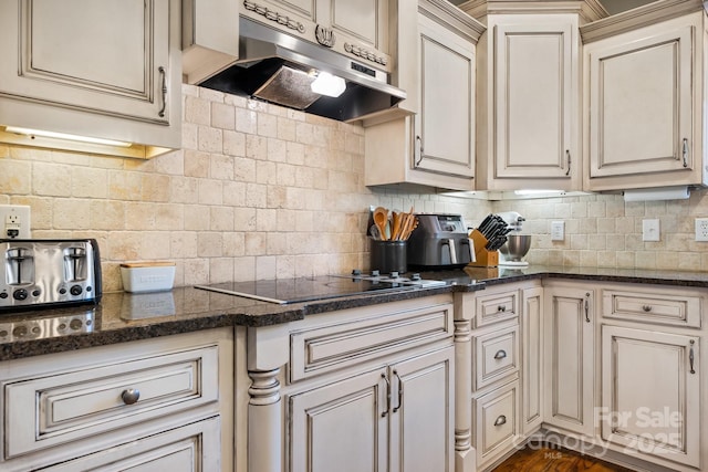 kitchen featuring dark stone counters, black electric stovetop, and backsplash