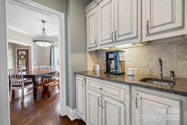 kitchen with sink, decorative backsplash, dark stone counters, crown molding, and dark wood-type flooring