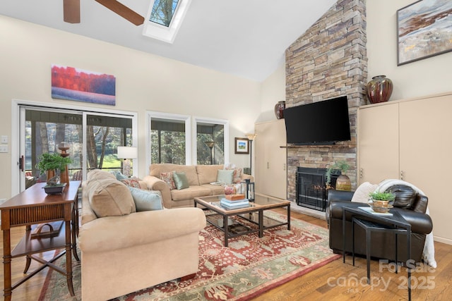 living room featuring ceiling fan, a fireplace, hardwood / wood-style flooring, a skylight, and high vaulted ceiling