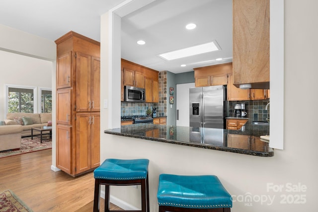 kitchen with stainless steel appliances, tasteful backsplash, dark stone countertops, kitchen peninsula, and a breakfast bar