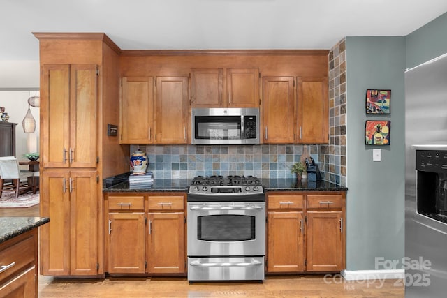 kitchen with decorative backsplash, appliances with stainless steel finishes, dark stone countertops, and light hardwood / wood-style floors