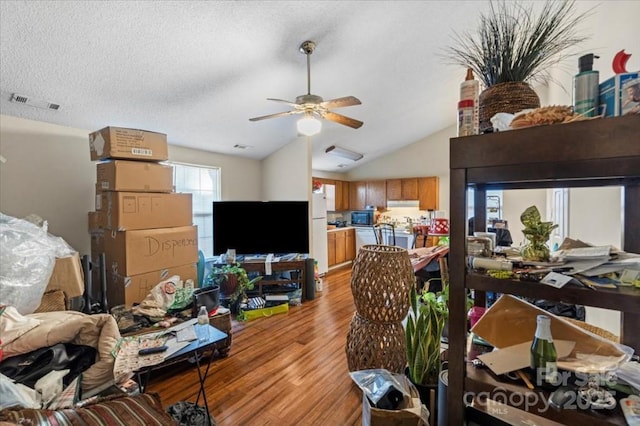 living room with ceiling fan, light wood-type flooring, lofted ceiling, and a textured ceiling