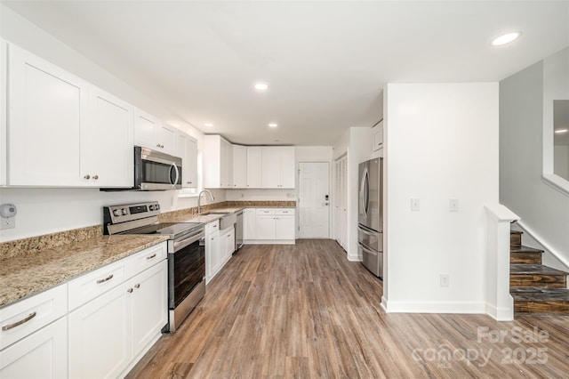 kitchen with light stone counters, white cabinets, appliances with stainless steel finishes, and sink