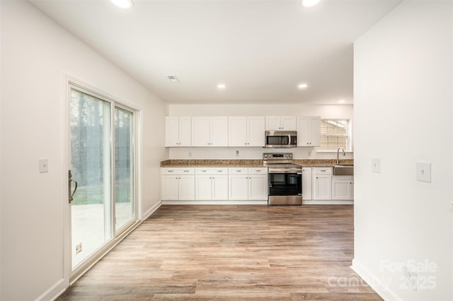 kitchen featuring light wood-type flooring, stainless steel appliances, a healthy amount of sunlight, and white cabinetry