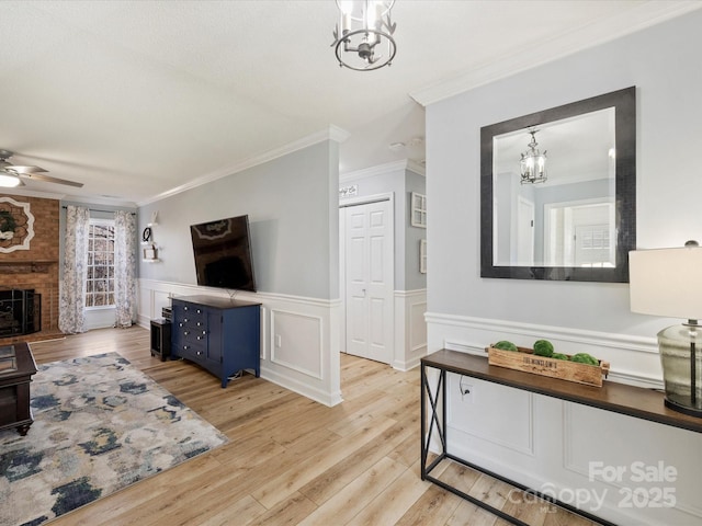 living room featuring ceiling fan with notable chandelier, ornamental molding, a fireplace, and light hardwood / wood-style flooring