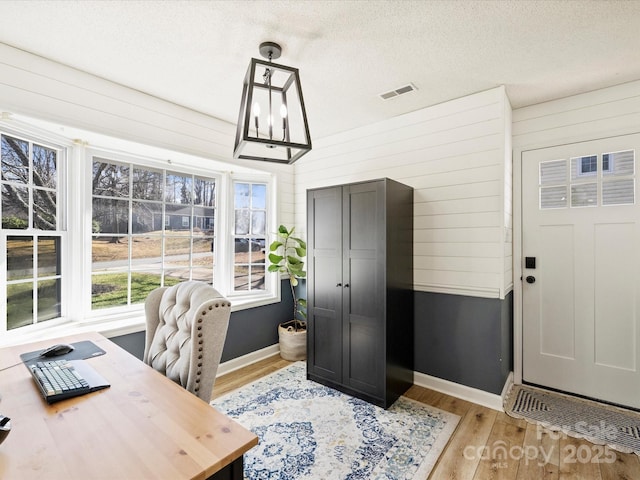 home office with light hardwood / wood-style floors, a textured ceiling, wood walls, and a chandelier