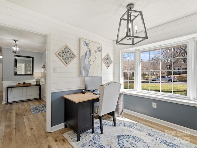 office featuring a notable chandelier, wooden walls, a textured ceiling, and light hardwood / wood-style floors