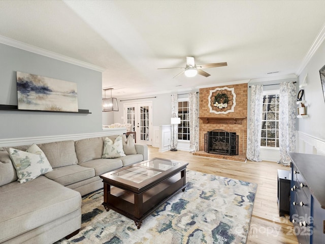 living room featuring french doors, a fireplace, ornamental molding, and light hardwood / wood-style flooring