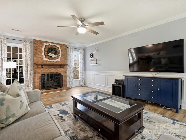 living room with ceiling fan, light wood-type flooring, a fireplace, and ornamental molding