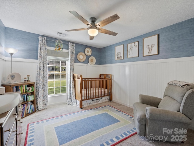 carpeted bedroom featuring ceiling fan, a crib, and a textured ceiling