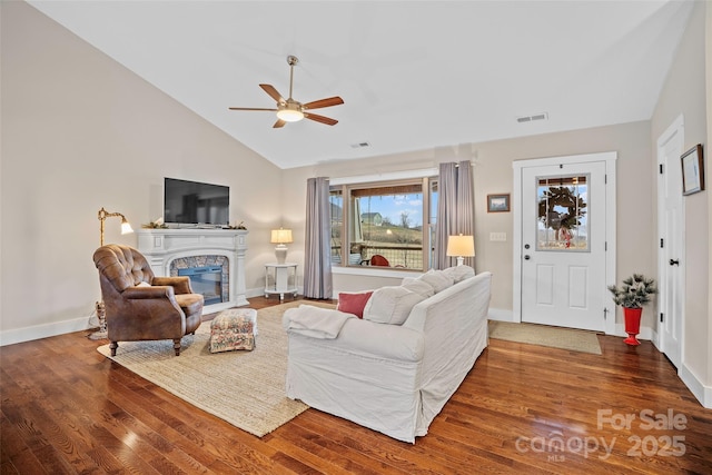 living room with dark hardwood / wood-style flooring, a stone fireplace, vaulted ceiling, and ceiling fan