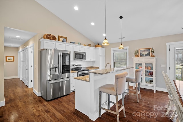 kitchen featuring appliances with stainless steel finishes, decorative light fixtures, white cabinets, light stone countertops, and a center island with sink