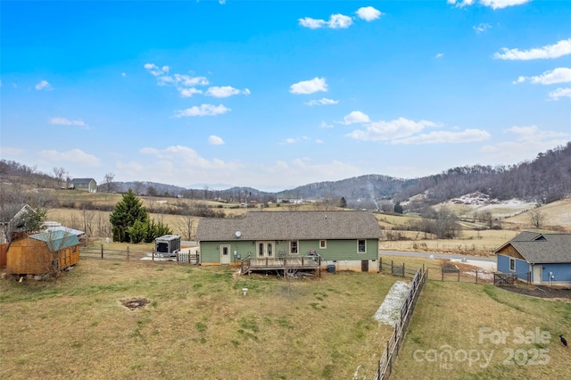 back of house featuring a storage unit, a deck with mountain view, a lawn, and a rural view