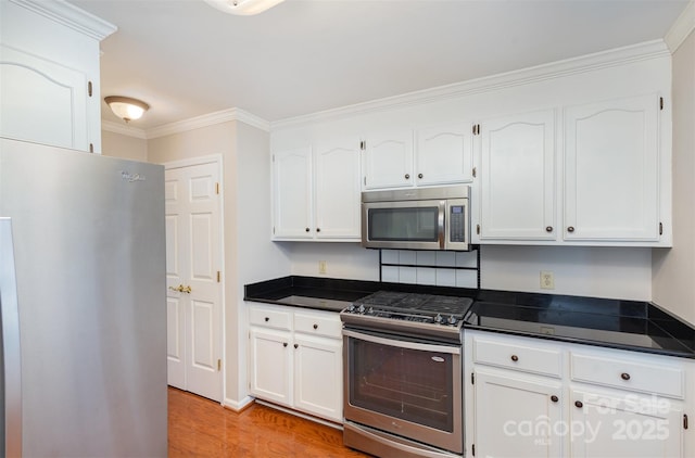 kitchen with white cabinetry, ornamental molding, appliances with stainless steel finishes, and light hardwood / wood-style flooring