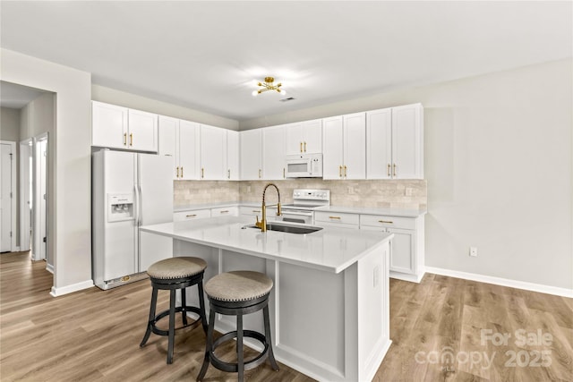 kitchen with white cabinetry, sink, a kitchen island with sink, and white appliances