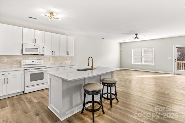 kitchen featuring sink, white appliances, light hardwood / wood-style flooring, an island with sink, and white cabinets