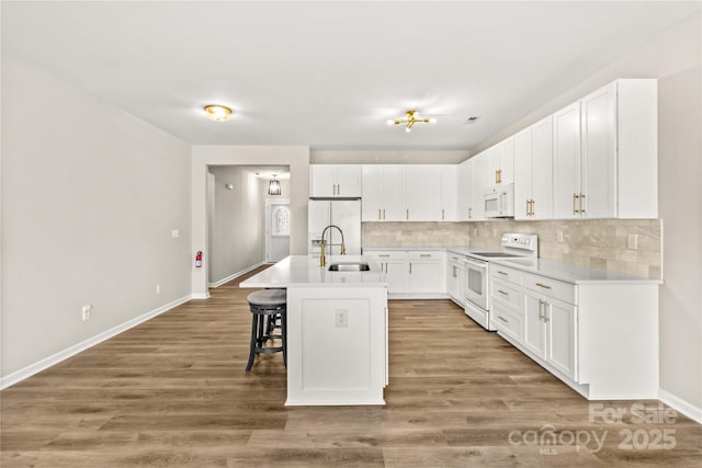 kitchen with white cabinetry, an island with sink, sink, a breakfast bar area, and white appliances