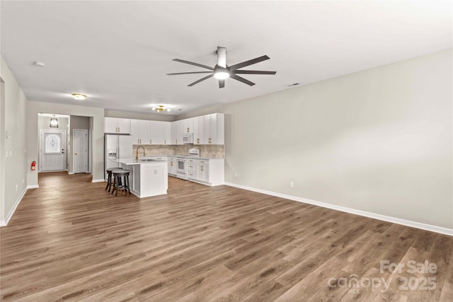 kitchen featuring white appliances, a breakfast bar area, white cabinetry, a center island with sink, and decorative backsplash