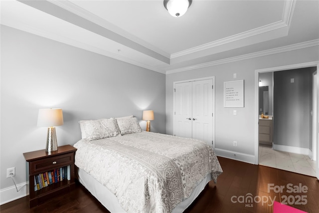 bedroom featuring a closet, ornamental molding, dark hardwood / wood-style flooring, and a tray ceiling