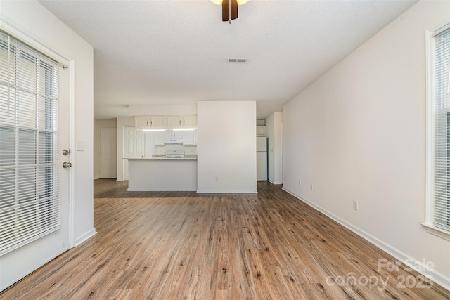 unfurnished living room featuring a textured ceiling, ceiling fan, light wood-type flooring, and plenty of natural light