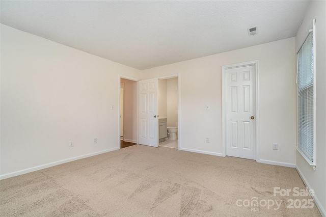 unfurnished bedroom with ensuite bath and light colored carpet