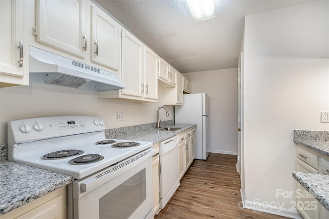 kitchen featuring under cabinet range hood, white appliances, wood finished floors, a sink, and light stone countertops