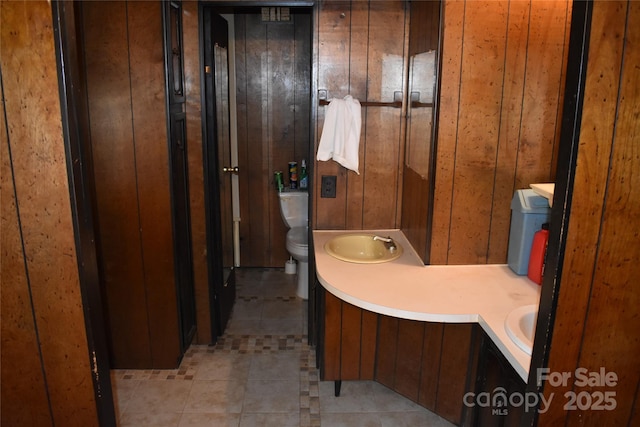 bathroom featuring tile patterned flooring, vanity, wood walls, and toilet