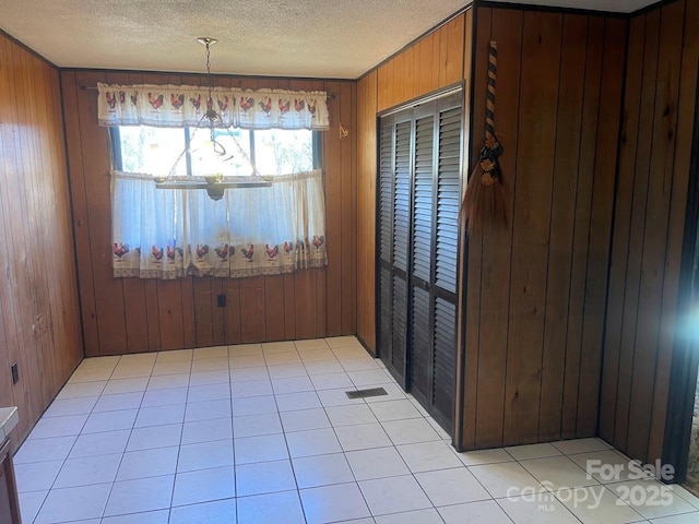 unfurnished dining area with light tile patterned floors, a textured ceiling, and wood walls