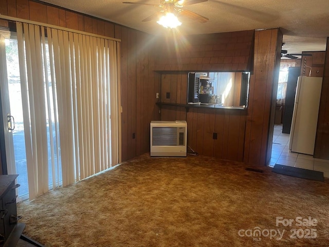 unfurnished living room featuring ceiling fan, wooden walls, carpet flooring, heating unit, and a textured ceiling