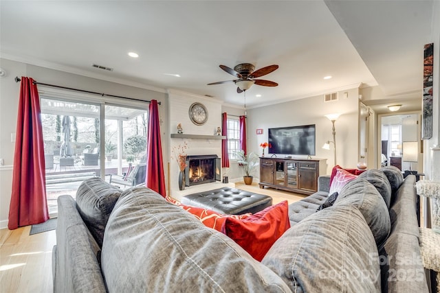 living room with ornamental molding, a large fireplace, ceiling fan, and light hardwood / wood-style flooring