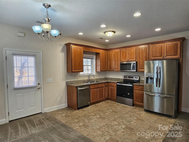 kitchen with sink, appliances with stainless steel finishes, a textured ceiling, decorative light fixtures, and dark stone counters