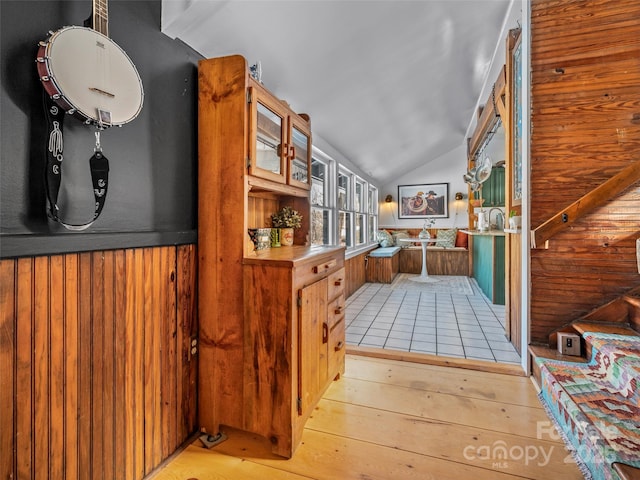 corridor featuring wooden walls, vaulted ceiling, and light hardwood / wood-style flooring