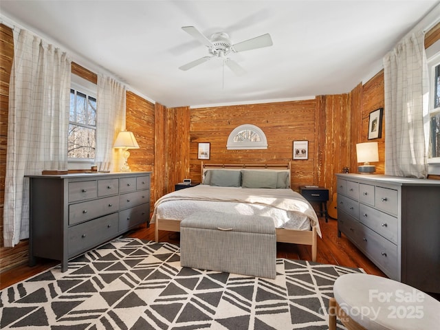 bedroom featuring ceiling fan, dark hardwood / wood-style flooring, and wooden walls