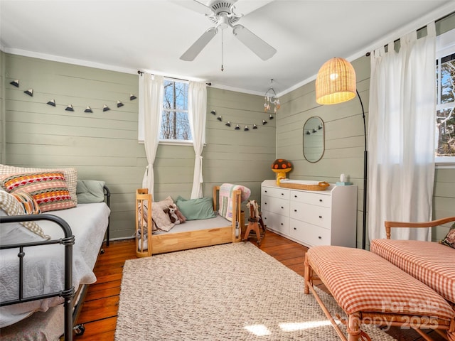 living area with ceiling fan, wood walls, crown molding, and dark hardwood / wood-style floors