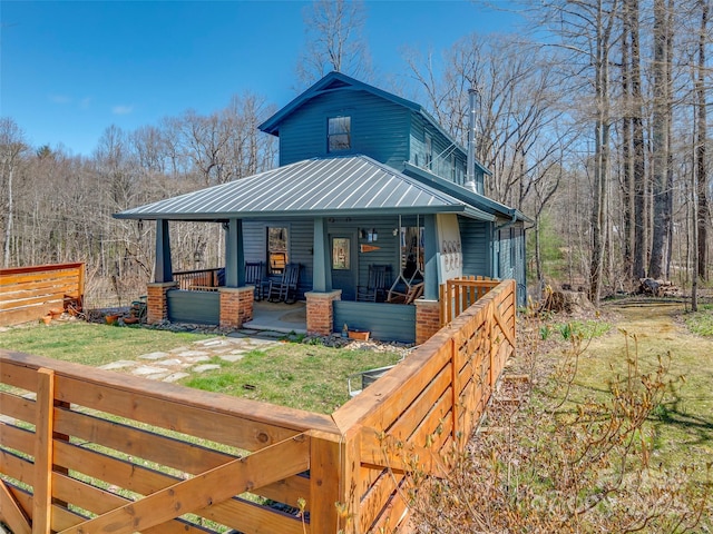 view of front facade featuring a porch, metal roof, a front lawn, and fence