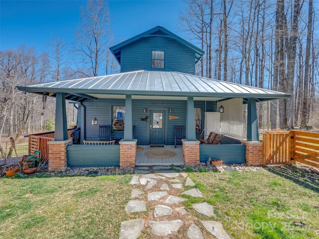 view of front of property featuring metal roof, covered porch, a front yard, and a standing seam roof