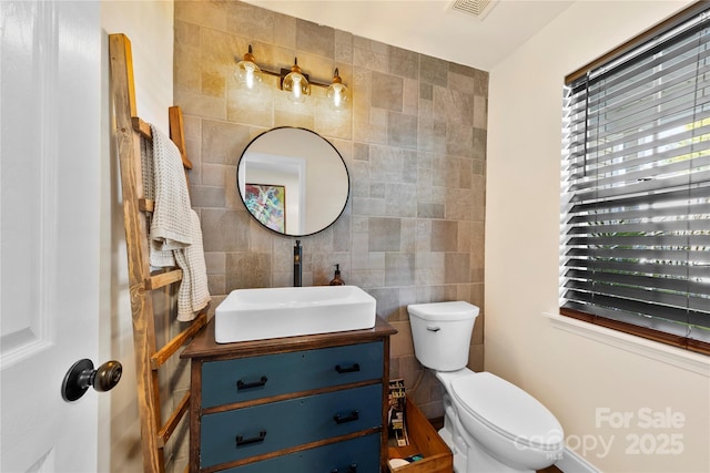 bathroom with toilet, vanity, and tile walls