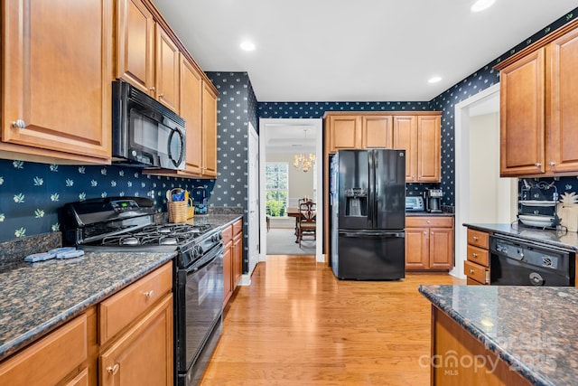 kitchen featuring black appliances, light hardwood / wood-style flooring, and dark stone counters