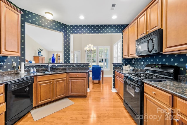 kitchen with black appliances, hanging light fixtures, light wood-type flooring, dark stone countertops, and sink