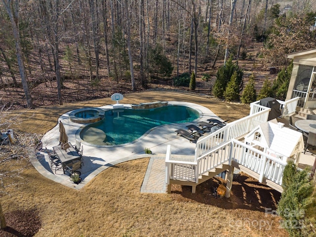 view of pool featuring a view of trees, area for grilling, a patio, a deck, and a pool with connected hot tub