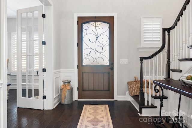 entryway with stairs, a decorative wall, dark wood-style flooring, and a wainscoted wall