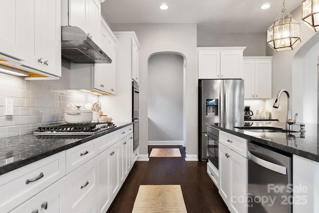 kitchen featuring arched walkways, appliances with stainless steel finishes, white cabinetry, a sink, and exhaust hood