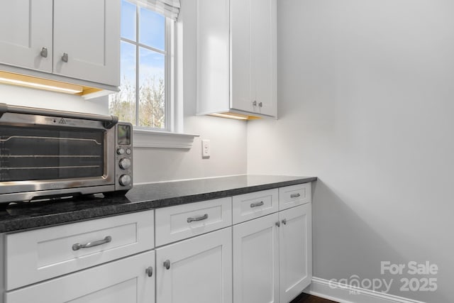 kitchen featuring baseboards, a toaster, white cabinetry, and dark stone countertops