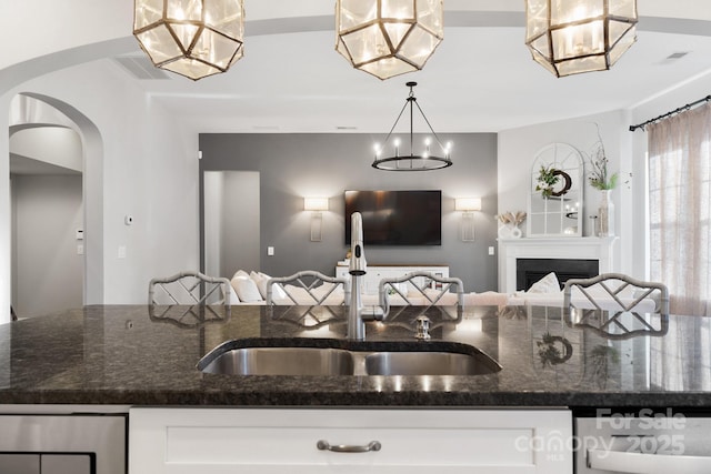 kitchen with dark stone countertops, white cabinetry, open floor plan, and a sink