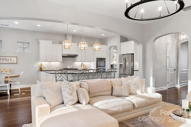 living room featuring baseboards, arched walkways, dark wood finished floors, and recessed lighting