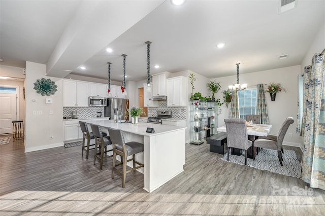 kitchen with appliances with stainless steel finishes, white cabinetry, hanging light fixtures, a kitchen island with sink, and an inviting chandelier