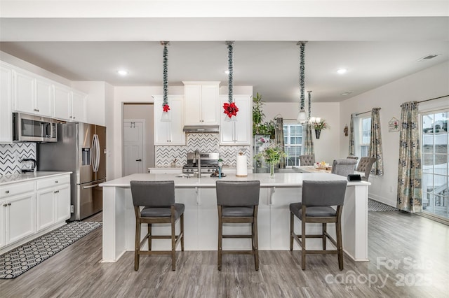 kitchen featuring white cabinetry, appliances with stainless steel finishes, a center island with sink, and decorative backsplash