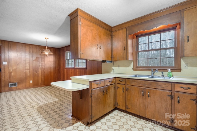 kitchen with wooden walls, decorative light fixtures, sink, kitchen peninsula, and a textured ceiling