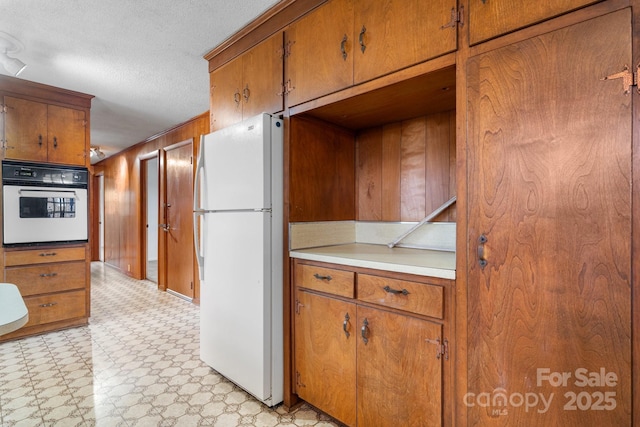 kitchen featuring a textured ceiling, white appliances, and wood walls